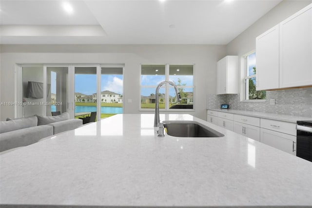 kitchen featuring backsplash, white cabinets, a water view, sink, and light stone countertops