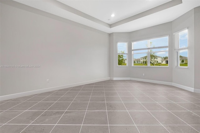 tiled empty room featuring a raised ceiling