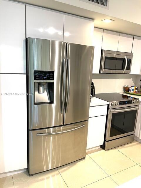 kitchen with stainless steel appliances, white cabinetry, and light tile patterned flooring