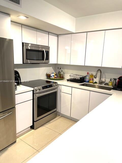 kitchen with white cabinets, light tile patterned floors, sink, and appliances with stainless steel finishes