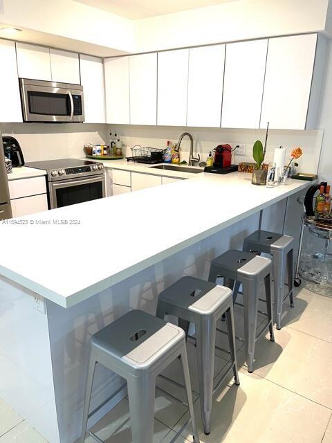 kitchen with a breakfast bar, sink, kitchen peninsula, white cabinetry, and stainless steel appliances