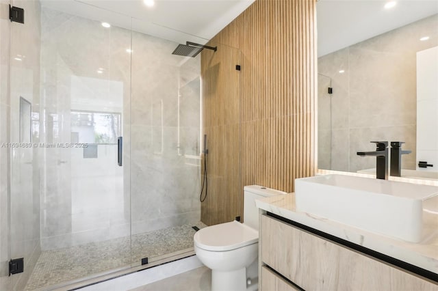 bathroom featuring vanity, toilet, a shower with shower door, and tile walls