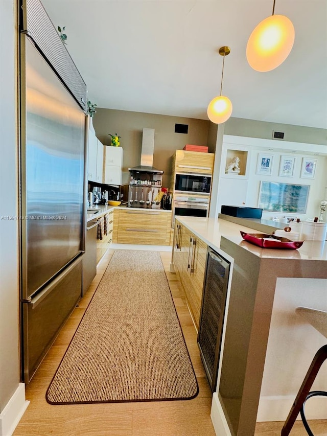 kitchen featuring built in appliances, decorative light fixtures, wine cooler, and wall chimney exhaust hood