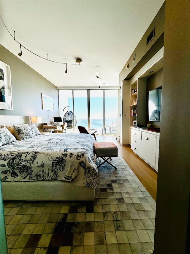 bedroom with dark hardwood / wood-style flooring, rail lighting, and a wall of windows