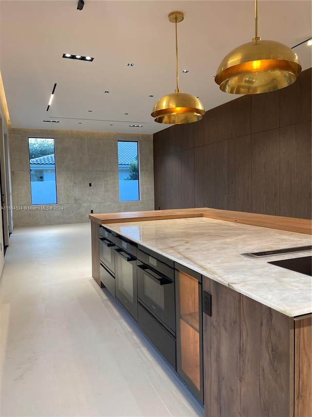 kitchen with light stone countertops, decorative light fixtures, a wealth of natural light, and tile walls