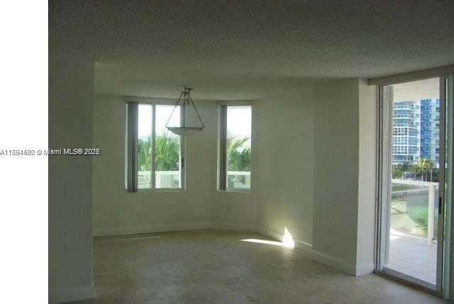 spare room featuring concrete flooring, plenty of natural light, a textured ceiling, and baseboards