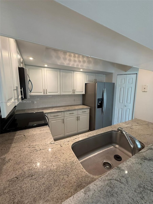 kitchen with tasteful backsplash, light stone countertops, white cabinets, and appliances with stainless steel finishes