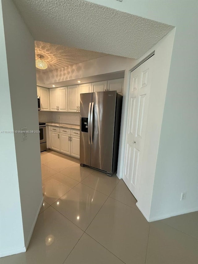 kitchen with light tile patterned floors, white cabinets, stainless steel appliances, and a textured ceiling