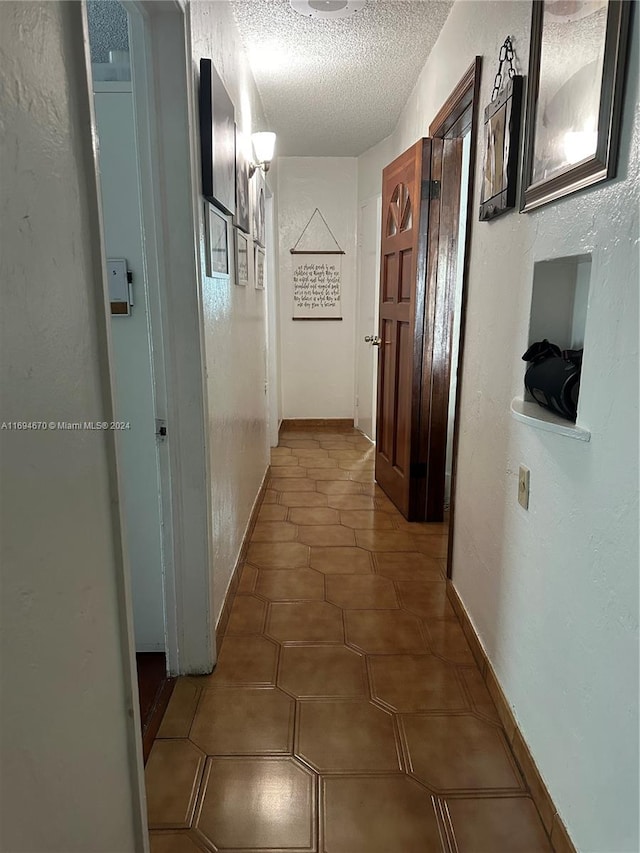 hall featuring a textured ceiling and dark tile patterned floors