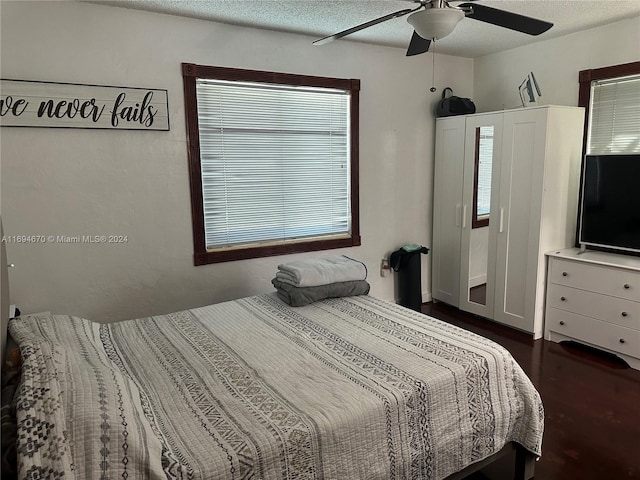 bedroom with a textured ceiling, ceiling fan, and dark wood-type flooring