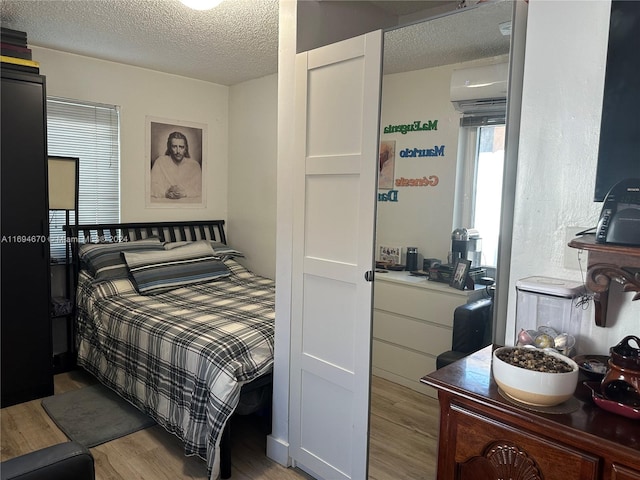 bedroom featuring a wall mounted air conditioner, a textured ceiling, and light hardwood / wood-style flooring