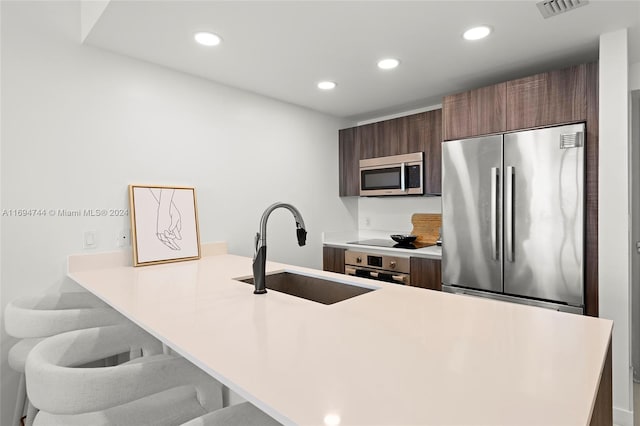 kitchen featuring kitchen peninsula, sink, appliances with stainless steel finishes, and a breakfast bar area