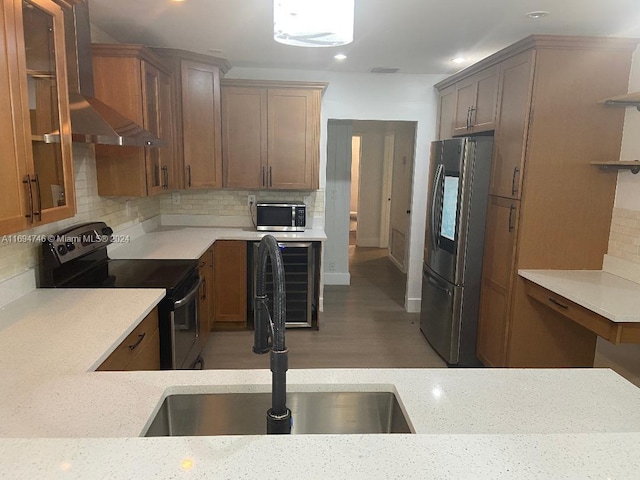 kitchen featuring light stone countertops, tasteful backsplash, stainless steel appliances, wall chimney range hood, and sink