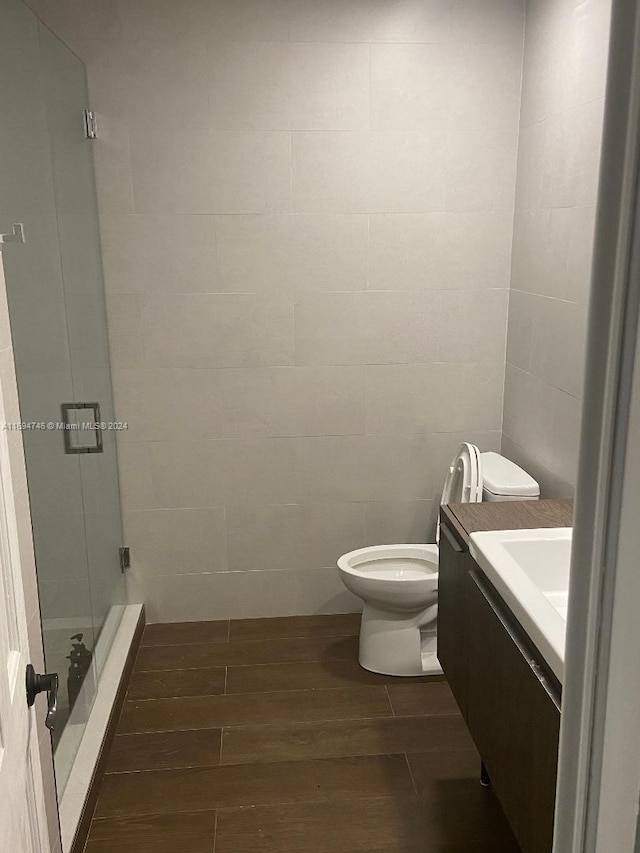 bathroom featuring vanity, hardwood / wood-style flooring, toilet, walk in shower, and tile walls