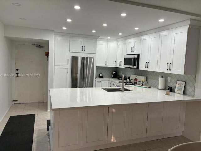 kitchen with stainless steel appliances, tasteful backsplash, light tile patterned flooring, kitchen peninsula, and white cabinets