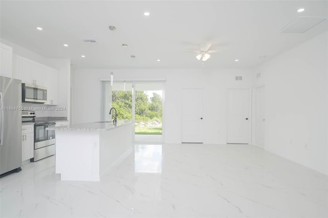 kitchen with light stone counters, stainless steel appliances, ceiling fan, a center island with sink, and white cabinetry