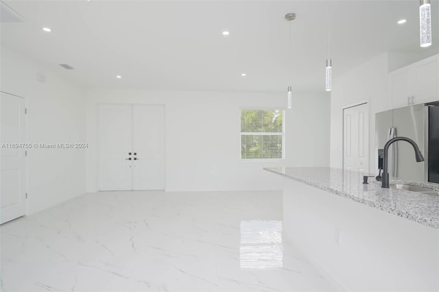 interior space featuring sink, stainless steel refrigerator with ice dispenser, light stone countertops, decorative light fixtures, and white cabinetry