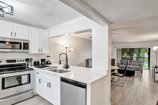 kitchen with sink, light wood-type flooring, appliances with stainless steel finishes, light stone counters, and white cabinetry