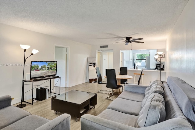 living room featuring ceiling fan, a textured ceiling, and light wood-type flooring