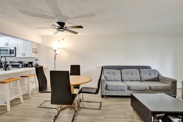 dining area with ceiling fan, light wood-type flooring, and a textured ceiling