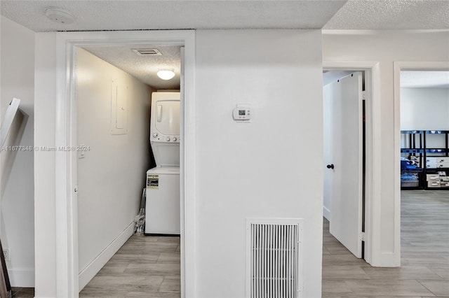 hallway with a textured ceiling, light wood-type flooring, and stacked washing maching and dryer