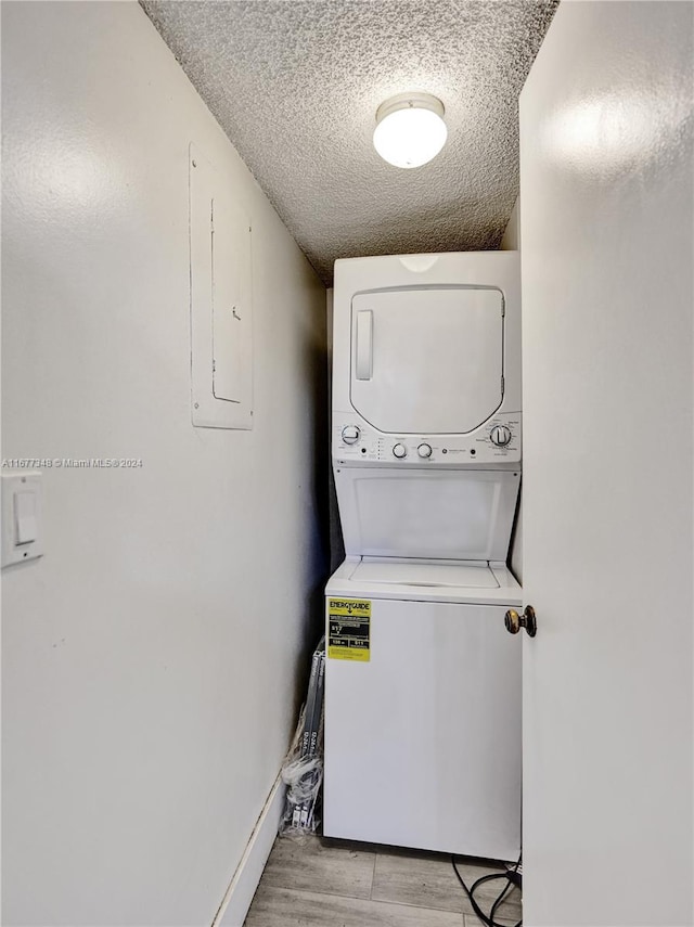 clothes washing area featuring a textured ceiling, light hardwood / wood-style floors, and stacked washer / drying machine