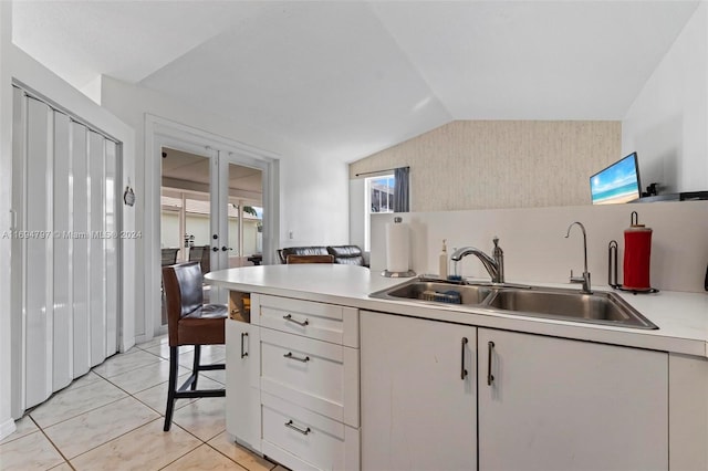 kitchen featuring sink, vaulted ceiling, light tile patterned floors, white cabinetry, and a breakfast bar area