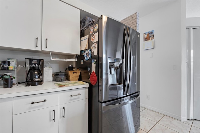 kitchen featuring baseboards, light countertops, stainless steel fridge, and white cabinets