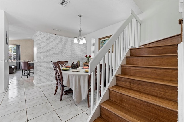 dining space featuring light tile patterned floors, visible vents, brick wall, stairway, and a chandelier