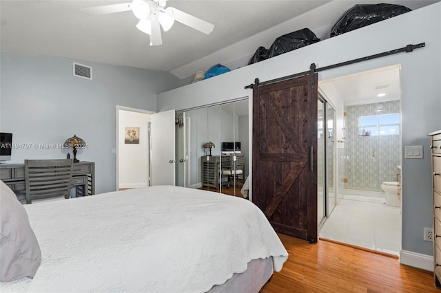 bedroom with ensuite bath, ceiling fan, a barn door, hardwood / wood-style flooring, and a closet