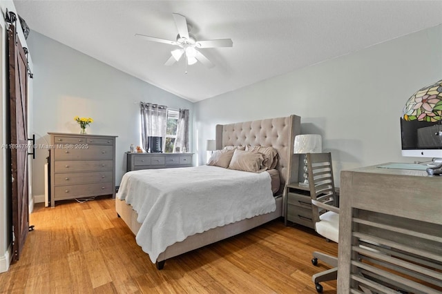 bedroom with a ceiling fan, vaulted ceiling, light wood-style flooring, and a barn door