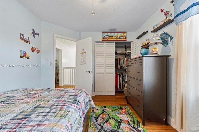 bedroom with light wood finished floors, a textured ceiling, visible vents, and a closet