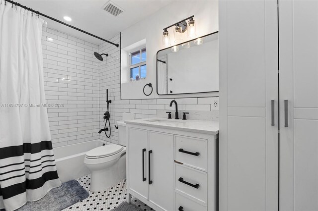 bathroom with toilet, vanity, visible vents, tile walls, and decorative backsplash