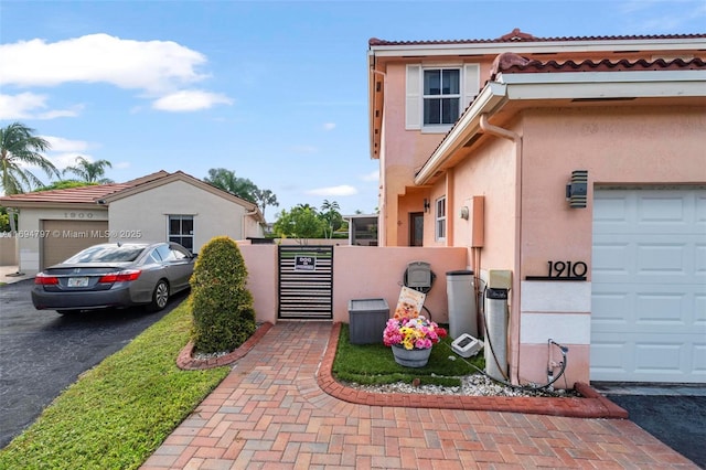 view of side of property featuring a garage, fence, decorative driveway, a gate, and stucco siding