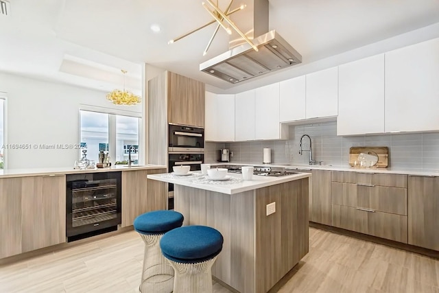 kitchen featuring island exhaust hood, light hardwood / wood-style flooring, white cabinets, a center island, and wine cooler