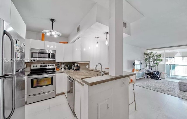 kitchen with kitchen peninsula, appliances with stainless steel finishes, backsplash, white cabinetry, and hanging light fixtures