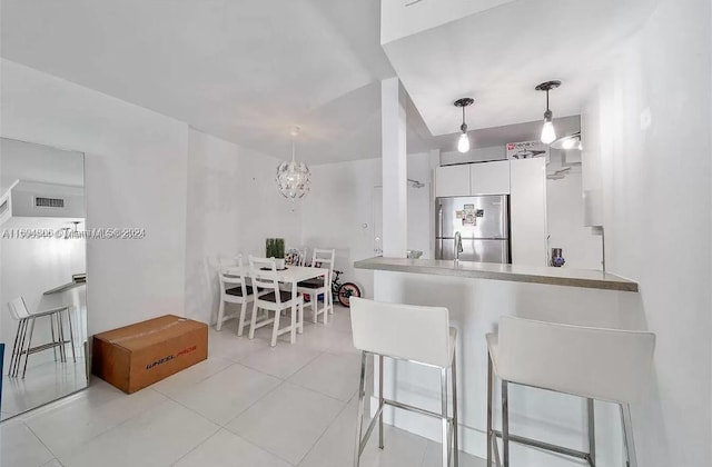 kitchen featuring a kitchen breakfast bar, a notable chandelier, stainless steel fridge, pendant lighting, and white cabinets