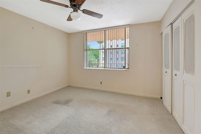 unfurnished bedroom with a textured ceiling, ceiling fan, light carpet, and a closet