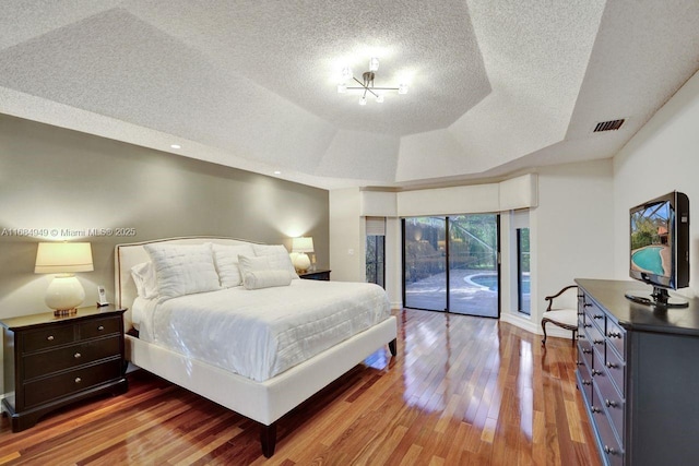 bedroom with a tray ceiling, access to exterior, and hardwood / wood-style floors