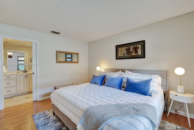 bedroom with a textured ceiling, light hardwood / wood-style flooring, and connected bathroom