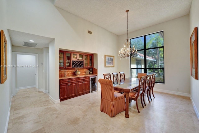 dining area featuring a towering ceiling, a textured ceiling, an inviting chandelier, bar area, and wine cooler