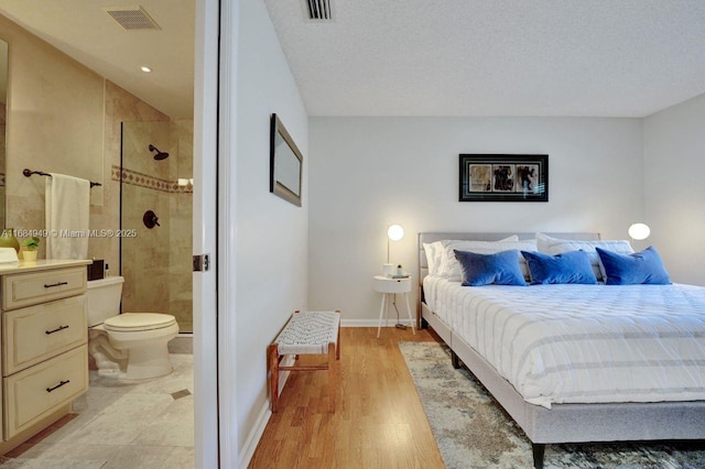 bedroom with light hardwood / wood-style floors, a textured ceiling, and ensuite bath