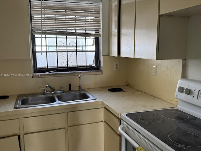 kitchen with electric stove, sink, and cream cabinets