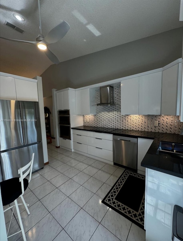 kitchen featuring lofted ceiling, wall chimney range hood, tasteful backsplash, white cabinetry, and stainless steel appliances