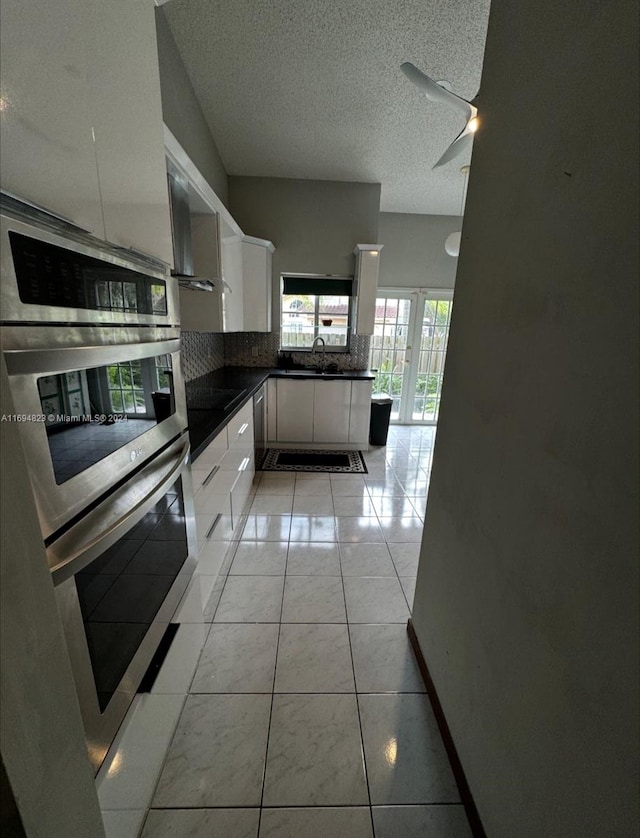 kitchen featuring double oven, light tile patterned floors, white cabinets, and a textured ceiling