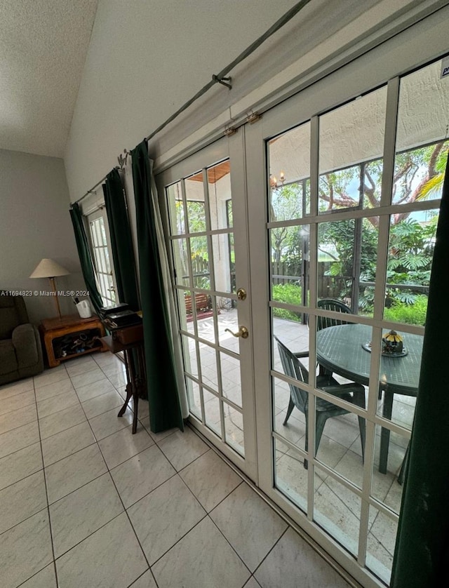 doorway with french doors, light tile patterned floors, a textured ceiling, and vaulted ceiling