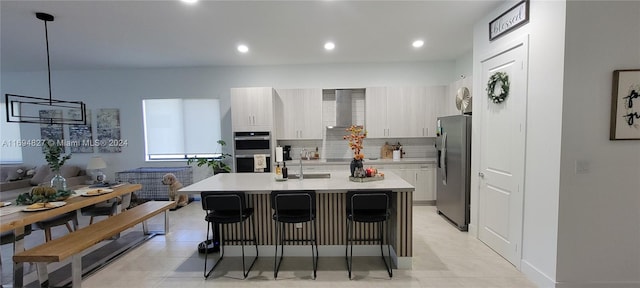 kitchen with pendant lighting, a kitchen breakfast bar, wall chimney range hood, an island with sink, and stainless steel appliances