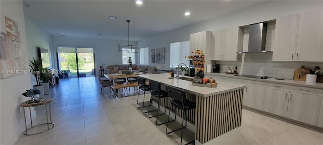 kitchen with a breakfast bar, pendant lighting, a center island with sink, and wall chimney range hood