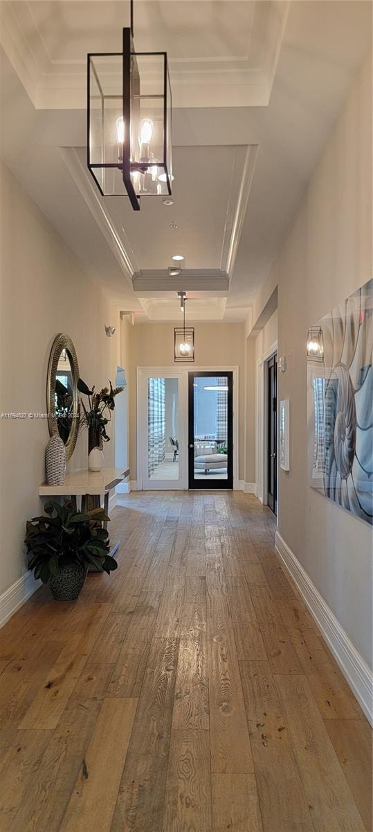 corridor with hardwood / wood-style flooring, a chandelier, ornamental molding, and a tray ceiling