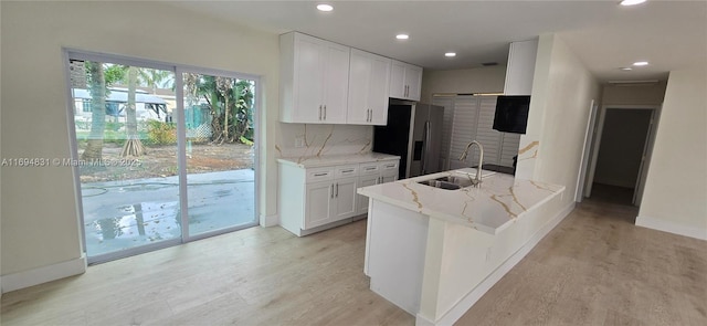 kitchen featuring white cabinetry, sink, light stone countertops, light hardwood / wood-style flooring, and decorative backsplash